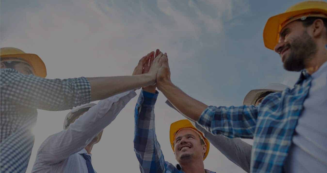 Construction team in hard hats high-fiving outdoors under blue sky