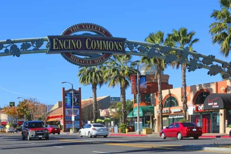 Encino, CA 1 Street view of Encino Commons shopping center with 'The Valleys Miracle Mile' sign, palm trees, and Verizon storefront