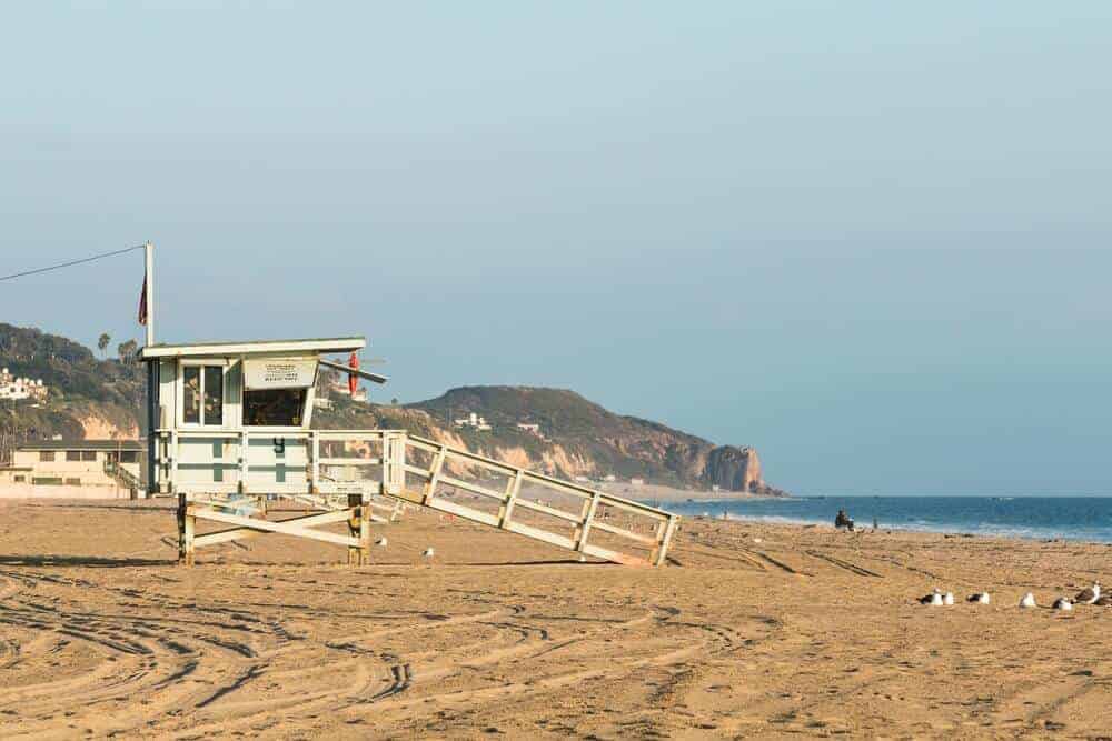 Malibu, CA 1 Lifeguard tower on sandy beach with ramp, calm ocean, seagulls, and cliffs under blue sky