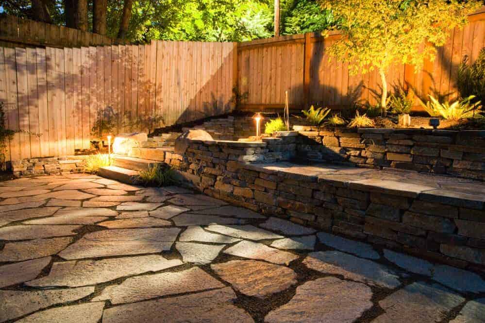 Brentwood, Los Angeles, CA 1 Serene nighttime patio with stone paving, warm lighting, and wooden fence